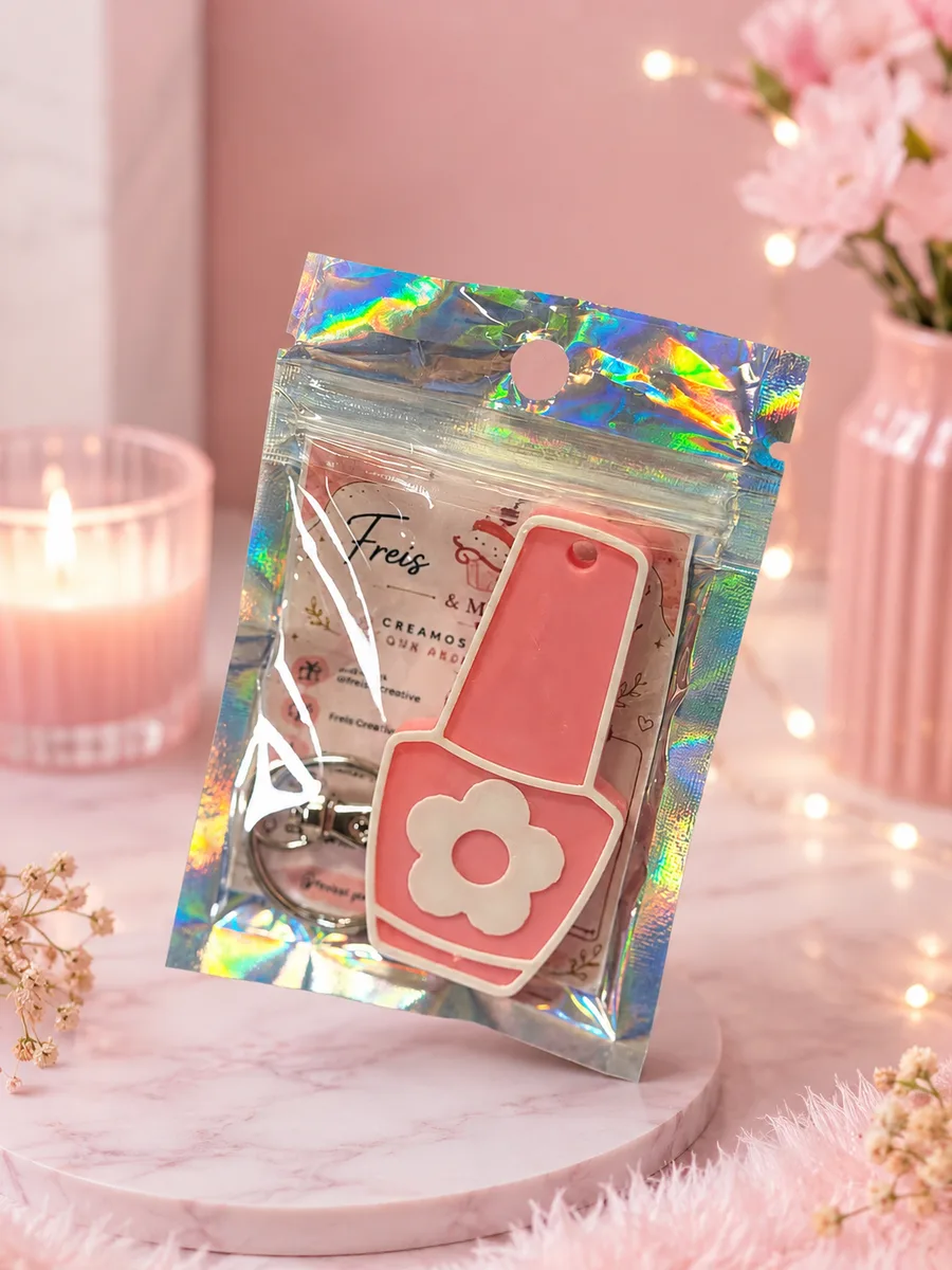 Llavero rosa con forma de bote de esmalte de uñas y detalle de flor blanca, en bolsa holográfica de regalo
